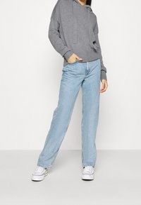 Grå hoodie med en avslappnad passform, ribbade ärmslut och en framficka, kombinerad med ljusblå raka jeans och vita sneakers.