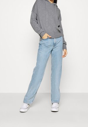 Sudadera gris con un corte relajado, puños acanalados y un bolsillo frontal, combinada con jeans rectos de un tono azul claro y zapatillas blancas.