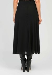 Jupe midi noire en tissu léger avec une forme évasée. Elle présente une texture lisse et tombe juste au-dessus du genou, assortie à des bottes noires.