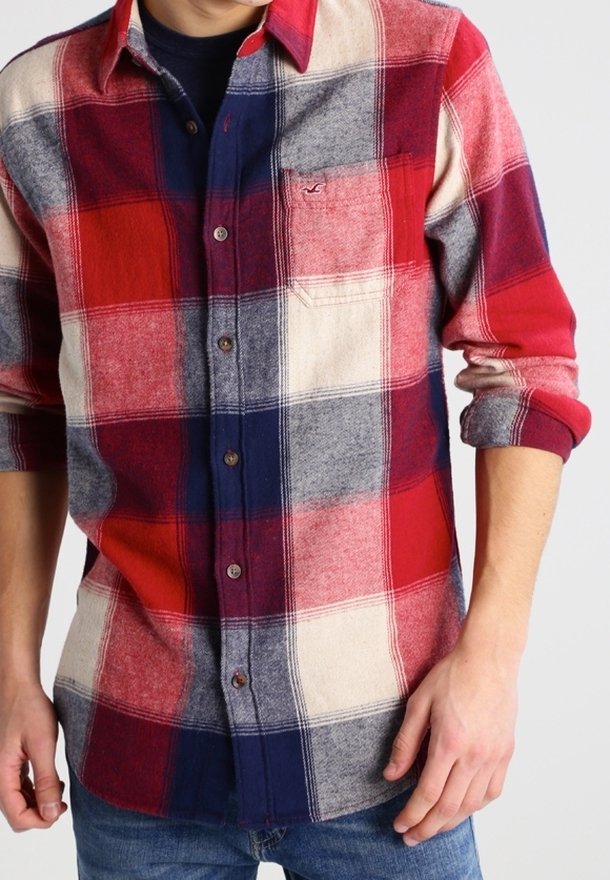 Karierte Flanellbluse in Rot, Marineblau und Creme mit langen Ärmeln, Knopfleiste und einer Brusttasche. Der Stoff fühlt sich weich an.