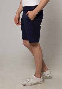 Tummansiniset puuvillahousut, joissa on sivutaskut, litteä etuosa ja rento istuvuus. Yhdistettynä valkoisiin tennareihin, joissa on raidallinen pohja.