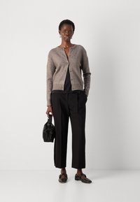 Lys brun strikket cardigan med knapper, sammen med en svart topp og svarte skreddersydde bukser. Tilbehør inkluderer en liten svart veske.