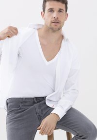 Weißes Hemd teilweise aufgeknöpft über einem weißen V-Ausschnitt-T-Shirt und grauen Slim-Fit-Jeans. Glatte Texturen und minimalistisches Design.