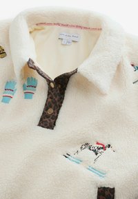 Krémový fleecový pulóver s leopardím vzorom na golieri, zdobený vyšívanými motívmi psa a rukavice. Obsahuje zlaté gombíky a hebkú textúru.