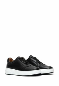 Zapatillas de cuero negro con una textura suave, punta redondeada y suela de goma blanca. Presentan costuras en contraste y cierre con cordones.