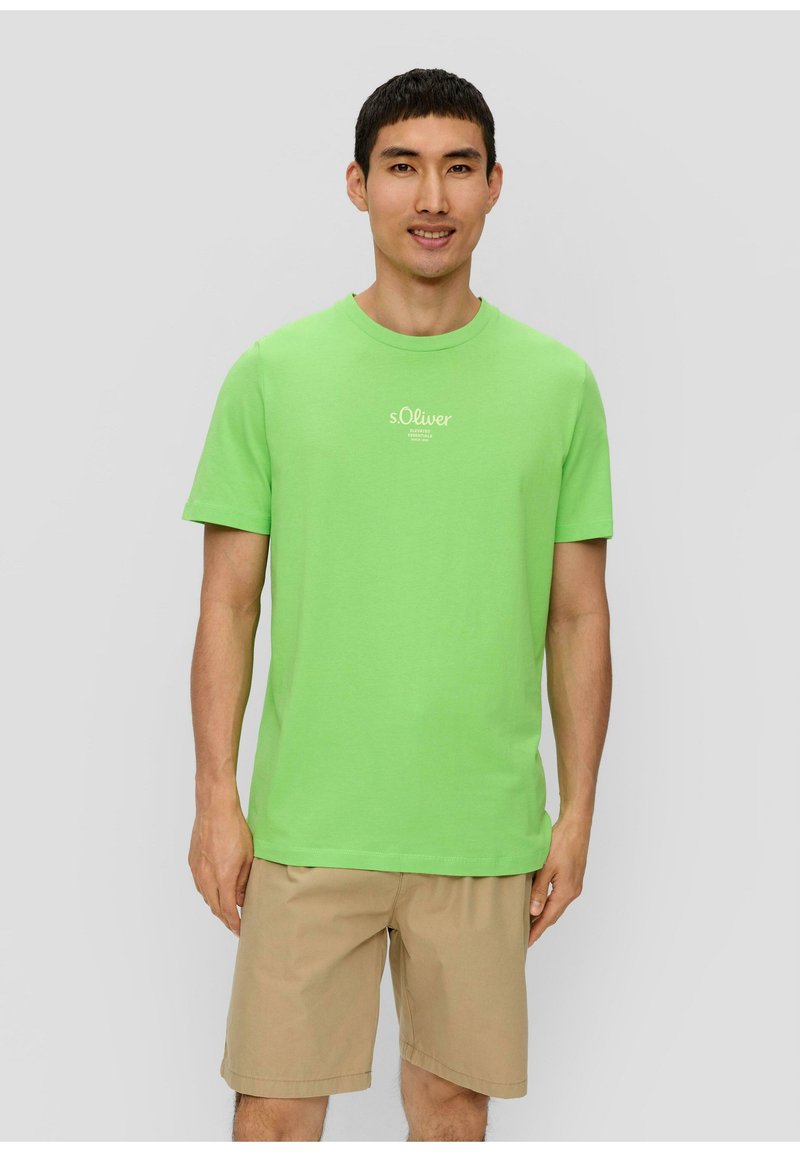 Grünes Baumwoll-T-Shirt mit kurzen Ärmeln, Rundhalsausschnitt und kleinem weißen Logo-Print auf der Brust. Das Modell trägt khakifarbene Shorts.