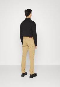 Musta lyhythihainen cropped-paita, joka on yhdistetty vaaleanbeigeihin housuihin ja mustiin kenkiin. Housuissa on näkyvä takatasku, jossa on logotagi.