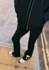 Fekete steppelt dzseki, fekete bővülő nadrág fehér madár- és csillagmintával a szegélyén, valamint világosszürke, hálós részletekkel ellátott sportcipő.