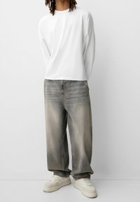 Valkoinen pitkähihainen paita, rento istuvuus, haalistuneet harmaat farkut ja beige tennarit sävyä korostavilla yksityiskohdilla, rento siluetti ja hienovarainen tekstuuri.