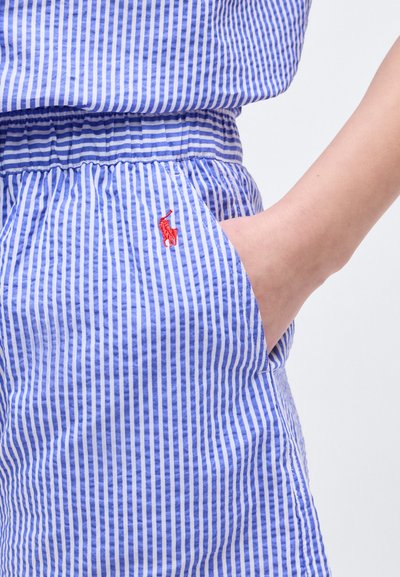 Χέρι στην τσέπη παντελονιού με κάθετες μπλε και λευκές ρίγες, ελαστική μέση και μικρό κόκκινο κεντημένο λογότυπο παίκτη πόλο.