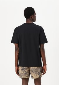 Sort kortærmet t-shirt med rund hals, lavet af bomuld, med en afslappet pasform og glat tekstur, bæres med mønstrede beige shorts.