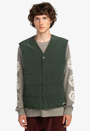 Gev quilted groene vest met een V-halslijn, drukknopen en een gestructureerde afwerking. Gedragen over een lange mouwen grijs shirt met graphics.
