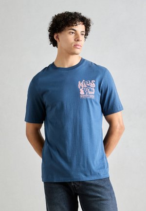 T-shirt en coton bleu à manches courtes avec un imprimé graphique rose sur la poitrine gauche, un col rond et une coupe décontractée, associé à un jean foncé.