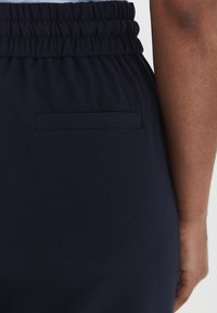 Navy blue fabric pants with an elastic waistband, featuring a single back pocket and a smooth texture. No visible patterns or accents.