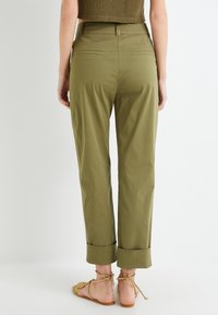 Pantalons vert olive à coupe droite, avec des ourlets à revers et deux poches arrière, associés à des sandales plates tan. Tissu léger.