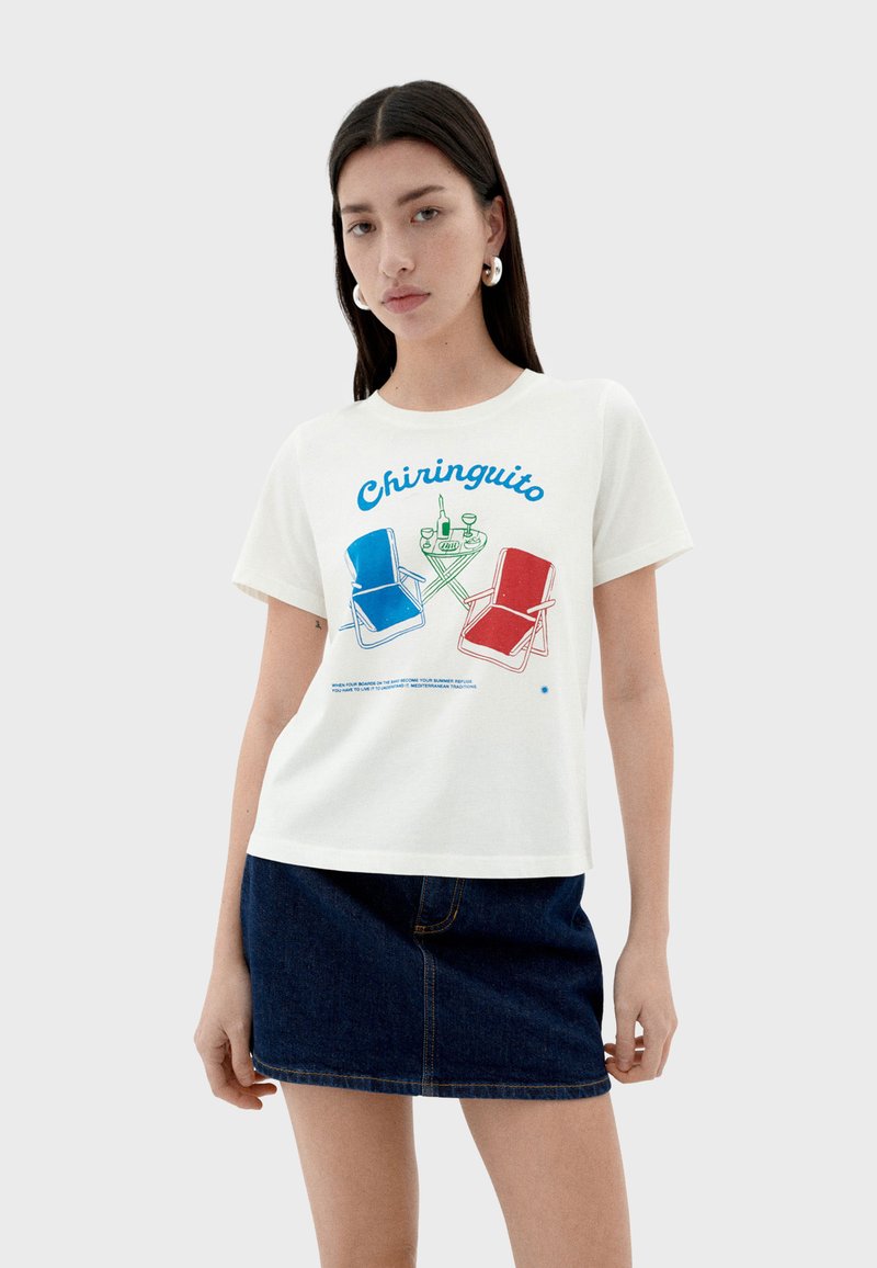 White cotton t-shirt featuring a colorful graphic of blue and red chairs, drinks, and "Chiringuito" text. Relaxed fit with short sleeves.