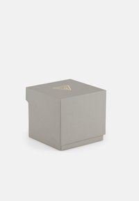 Boîte d'emballage grise avec une surface texturée. Présente un logo triangulaire doré sur le dessus. Forme carrée avec un couvercle pliable.