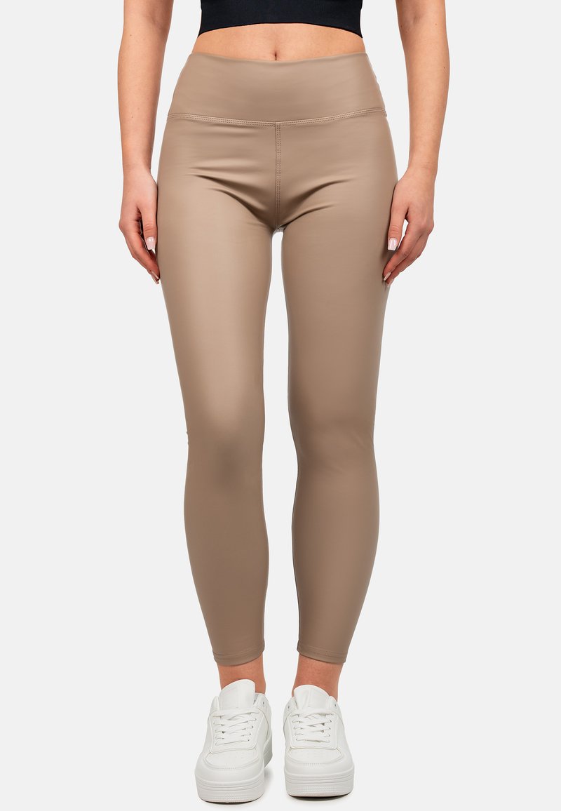 Leggings beige a vita alta realizzati in tessuto elasticizzato, caratterizzati da una superficie liscia e un design aderente, abbinati a sneakers bianche.