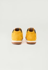 Gelbe Wildleder-Sneaker haben eine strukturierte Oberfläche, ein schwarzes Stofffutter und Gummisohlen, mit einem weißen und beige Akzent um die Sohle.