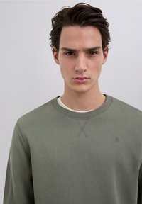 Olive green sweatshirt made of cotton blend, featuring a round neckline, textured stitching detail, and a small logo on the chest.
