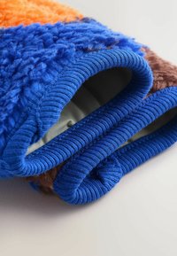 Futrzany materiał odzieżowy z pomarańczowymi, niebieskimi i brązowymi teksturami. Niebieskie prążkowane mankiety akcentują krawędzie, podkreślając jego przytulny design.
