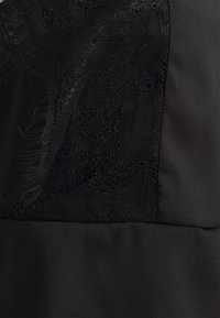 Détail en tissu noir mettant en avant un panneau en dentelle avec des motifs floraux et une texture satinée lisse. Couleur noire riche et profonde tout au long.