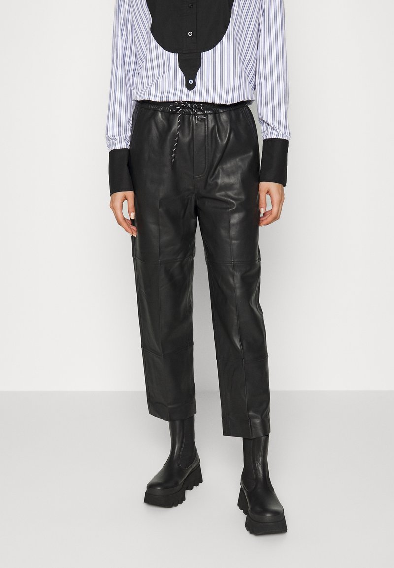 Schwarze Lederhosen mit lockerer Passform, ausgestattet mit einem elastischen Bund und zwei Seitentaschen. Kombiniert mit einem gestreiften Hemd mit Knopfleiste.