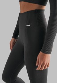 Sorte ribbede leggings med høy midje og en liten sølvlogo. Stoffet har en teksturert, kroppsnær design.
