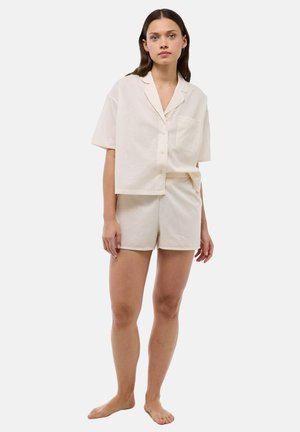Ensemble de vêtements d'intérieur en coton dans une teinte crème clair, comprenant une chemise à manches courtes avec boutons et poche, accompagnée de shorts assortis avec ourlets retournés.