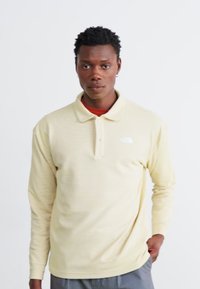 Langærmet polo-shirt i lys gul med subtile striber, med en krave-udskæring og et lille hvidt logo på brystet.