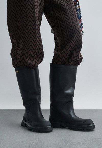 Svarta gummistövlar i knähöjd med texturerad finish, med en kraftig sula och enkel design. Pyntade med guldfärgad logotyp.