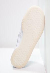 Vit idrottssko sula med en strukturerad gummiyta, som har ett cirkulärt mönster och varumärket "Reebok" präglat nära hälen.