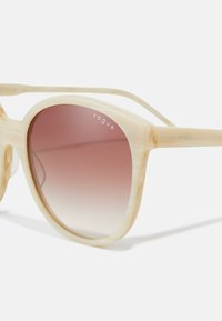 Γυαλιά ηλίου με λευκή επικάλυψη και κεκλιμένα ροζ φακούς. Χαρακτηριστικά περιλαμβάνουν στρογγυλό σκελετό και υφή στην πρόσοψη, με την επωνυμία 'vogue' στους βραχίονες.