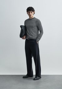 Gray patterned long-sleeve shirt, black trousers, and black shoes. Carrying a black textured clutch bag. Simple, modern design.