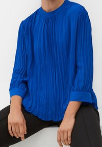 Top plissettato blu reale con maniche lunghe e scollatura rotonda. Presenta una texture arricciata e polsini solidi blu a contrasto.