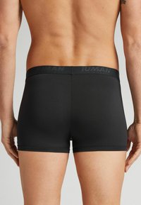 Schwarze Boxer-Briefs mit einem weichen Bund, der "HUMAN" trägt, körperbetontes Design, glatte Textur und ohne sichtbare Logos oder Muster.