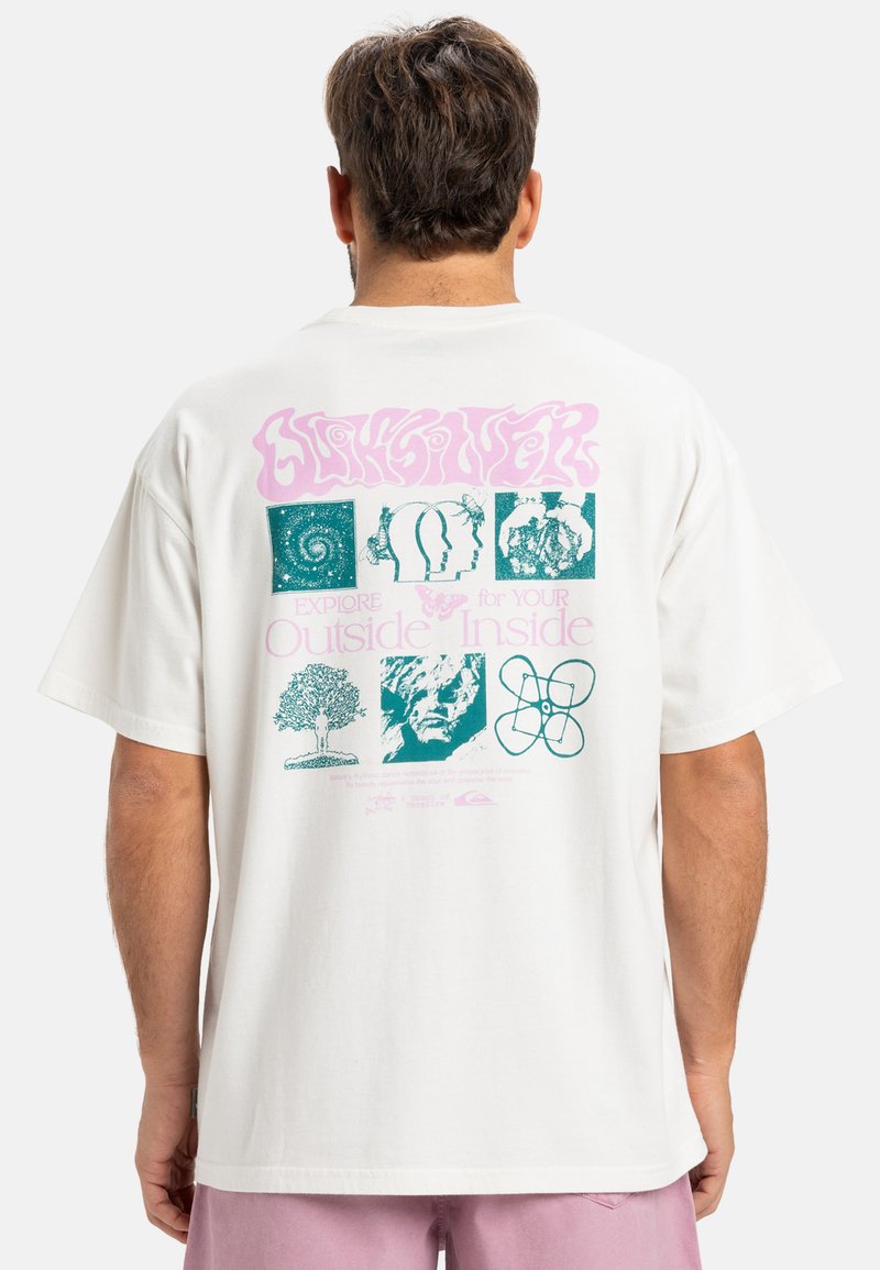 Hvid bomulds t-shirt med et stort flerfarvet grafik på bagsiden, der indeholder designs som træer, hoveder og abstrakte former.