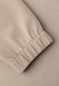 Funda de tela beige con detalle de puño elástico, mostrando una textura suave y lisa y costuras finas sobre un fondo a juego.