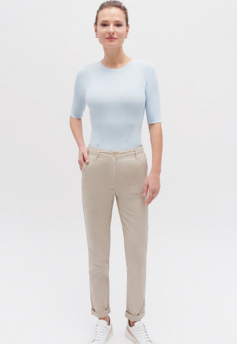 Lichtblauw geribbeld T-shirt met korte mouwen, gecombineerd met beige broeken, voorzien van een knoopsluiting, opgerolde mouwen en witte sneakers. Soepele textuur.