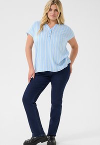 Blusa a rayas azul claro con cuello henley y mangas cortas, combinada con jeans azul oscuro y zapatos de plataforma negros.