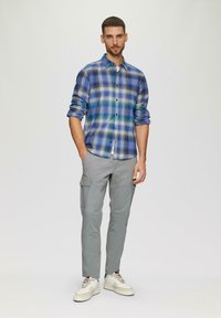Geruite button-up shirt in blauw en groene tinten, gecombineerd met lichtgrijze cargobroek. Schoeisel heeft een witte basis met subtiele accenten.