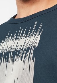 Mörkblå bomullströja med rund hals som har ett vitt abstrakt linjemönster. Tyget har en slät yta och en figurnära passform.