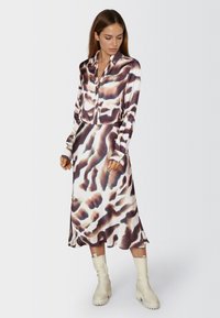 Silk button-up shirt and matching skirt in a brown and white abstract print. Slim fit with long sleeves and a smooth texture. Beige knee-high boots.