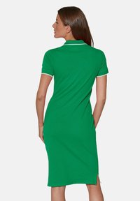 Grünes Polokleid mit kurzen Ärmeln, weißen Akzenten, geradem Schnitt, knielang und mit einem seitlichen Schlitz für Bewegungsfreiheit.