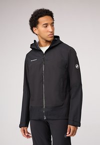 Chaqueta negra impermeable con capucha, que cuenta con cierre de cremallera, textura a cuadros en la sección superior y detalles de logo en el pecho y la manga.