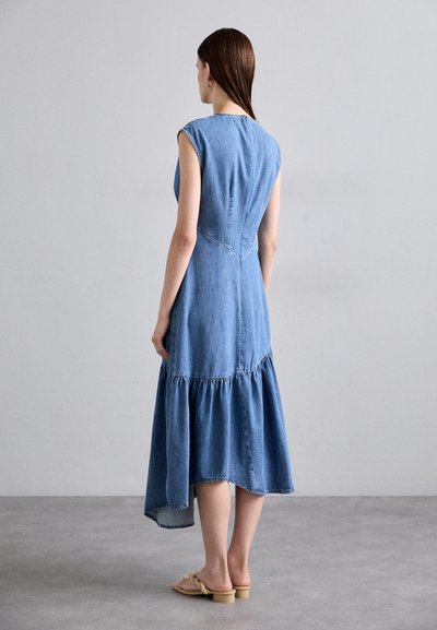 Denim jurk met een blauwe tint, korte mouwen, een getailleerde bodice en een uitlopende, gelaagde zoom op een asymmetrische lengte. Plat sandaal voor een casual uitstraling.