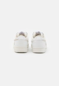 Hvite sneakers med et glatt skinnoverdel, lyse beige detaljer og en lav profil såle. Har en polstret krage og et minimalistisk design.