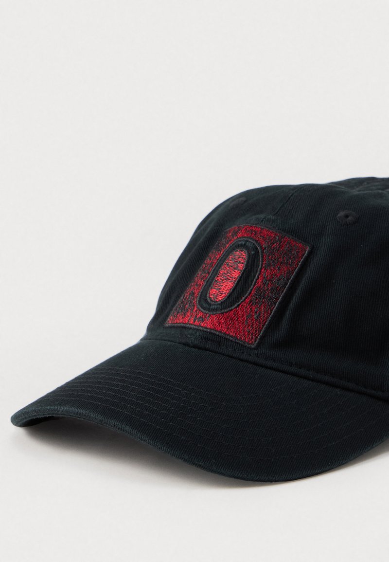 Schwarze Kappe mit einem strukturierten roten und schwarzen gestickten Logo auf einem rechteckigen Patch. Verfügt über einen gebogenen Schirm und einen verstellbaren Riemen auf der Rückseite.