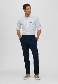 Wit en lichtblauw gestreept overhemd, opgerolde mouwen, gecombineerd met marineblauwe broek en tan sneakers. De stof lijkt soepel en lichtgewicht.