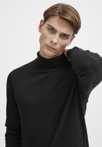 Maglione a collo alto nero realizzato in un tessuto morbido e leggero; presenta un colletto aderente e maniche lunghe con dettagli a coste.